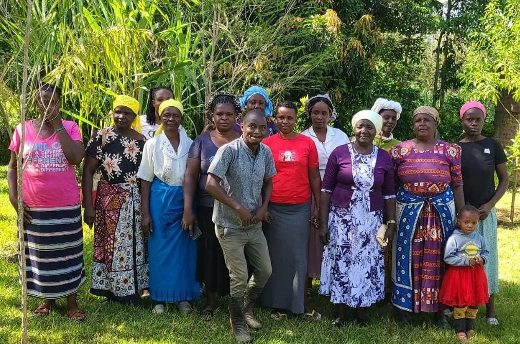 A group of women and one man standing together in a garden among tall grasses and trees